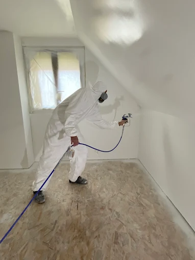 Peintre PRISME en combinaison appliquant la peinture au pistolet dans des combles